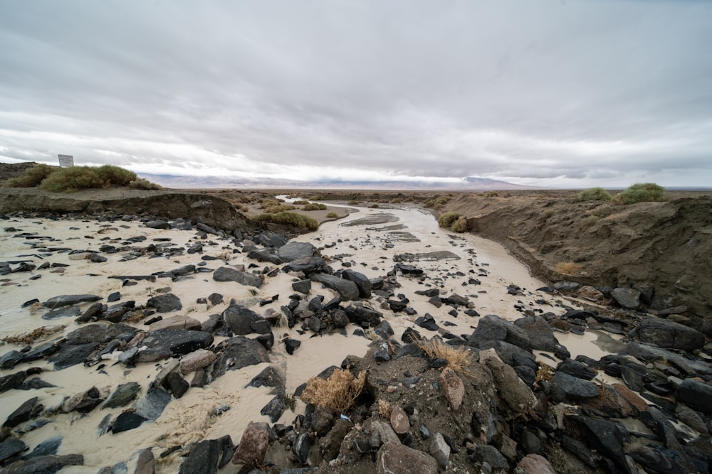 a sandy beach with rocks and water under a cloudy sky