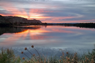 Sunset over a calm lake with reflections of trees.