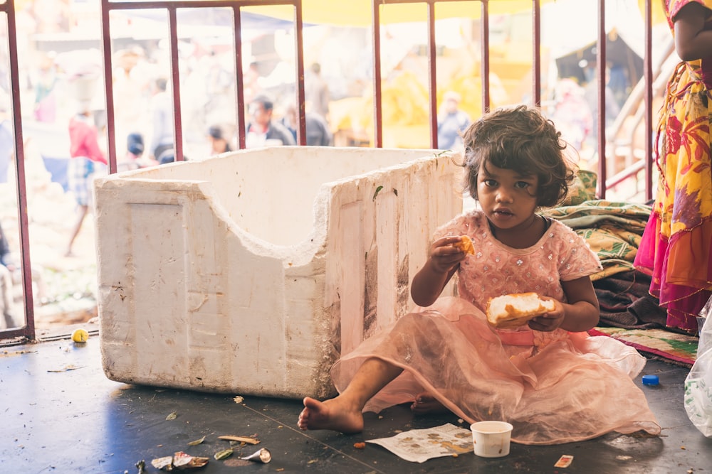 a little girl sitting on the ground eating food