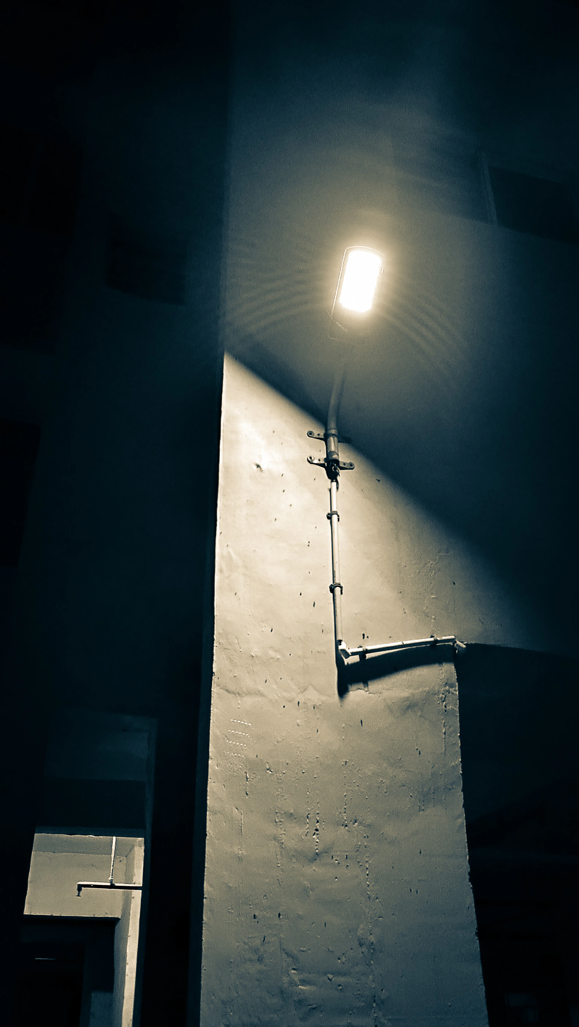 A striking black and white still from a moody urban night film scene featuring deep shadows and glowing street lamps.