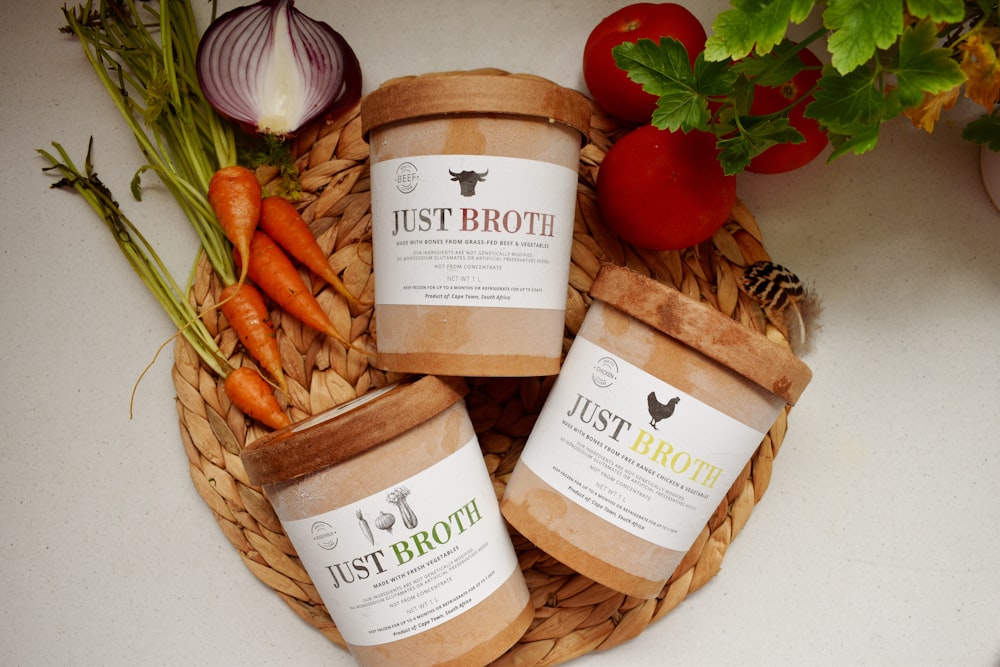 three jars of just broth sitting on a table next to vegetables