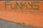 Graffiti on a concrete surface with the word 'FUN' painted in green over an orange background. The paint is applied in a bold, stylized font. The backdrop includes scattered dry leaves and a hint of a paved walkway.