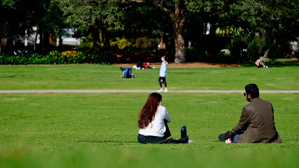 a couple of people sitting on top of a lush green field