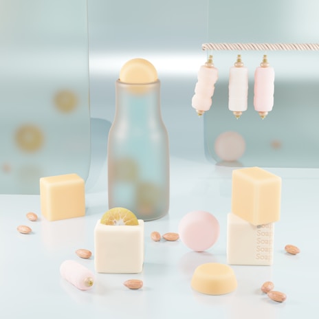 Aesthetic arrangement of pastel-colored objects on a glossy surface, featuring a frosted glass bottle with a spherical cap, cream and pale pink cylindrical objects hanging from a rope, and various bar soaps shaped as cubes with embossed text. Scattered almonds and a cut lime add visual interest.