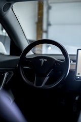 The interior of a car featuring a steering wheel with a logo in the center. A large touchscreen display is visible on the right side.