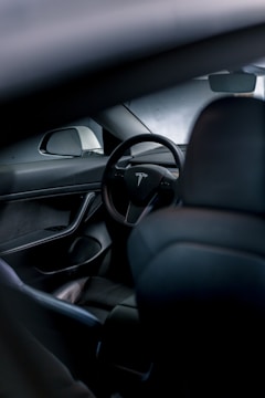 The interior of a car featuring a sleek, modern design with a prominent steering wheel displaying a logo. The focus is on the minimalist and high-tech dashboard, which includes a side mirror and smooth surfaces.