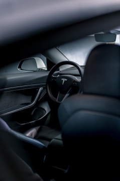 The interior of a car featuring a sleek, modern design with a prominent steering wheel displaying a logo. The focus is on the minimalist and high-tech dashboard, which includes a side mirror and smooth surfaces.