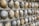 A close-up view of a textured wall constructed with smooth, rounded stones embedded in a concrete-like surface. The stones vary in color from gray to brown and are arranged in a uniform pattern.