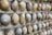 A close-up view of a textured wall constructed with smooth, rounded stones embedded in a concrete-like surface. The stones vary in color from gray to brown and are arranged in a uniform pattern.