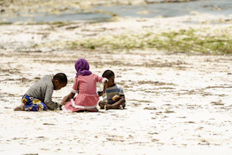 a group of children sitting on top of a sandy beach