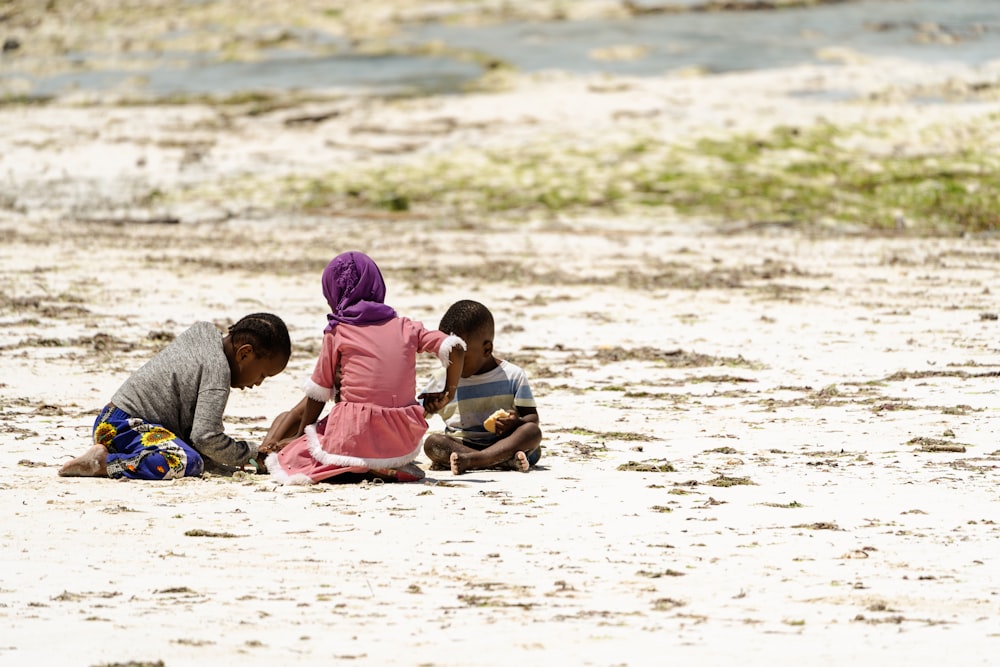 a group of children sitting on top of a sandy beach