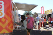 Smiling staff serving happy guests from a bustling food truck at a sunny festival.