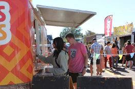 Smiling staff serving happy guests from a bustling food truck at a sunny festival.