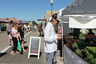 a man standing next to a sign at a farmers market