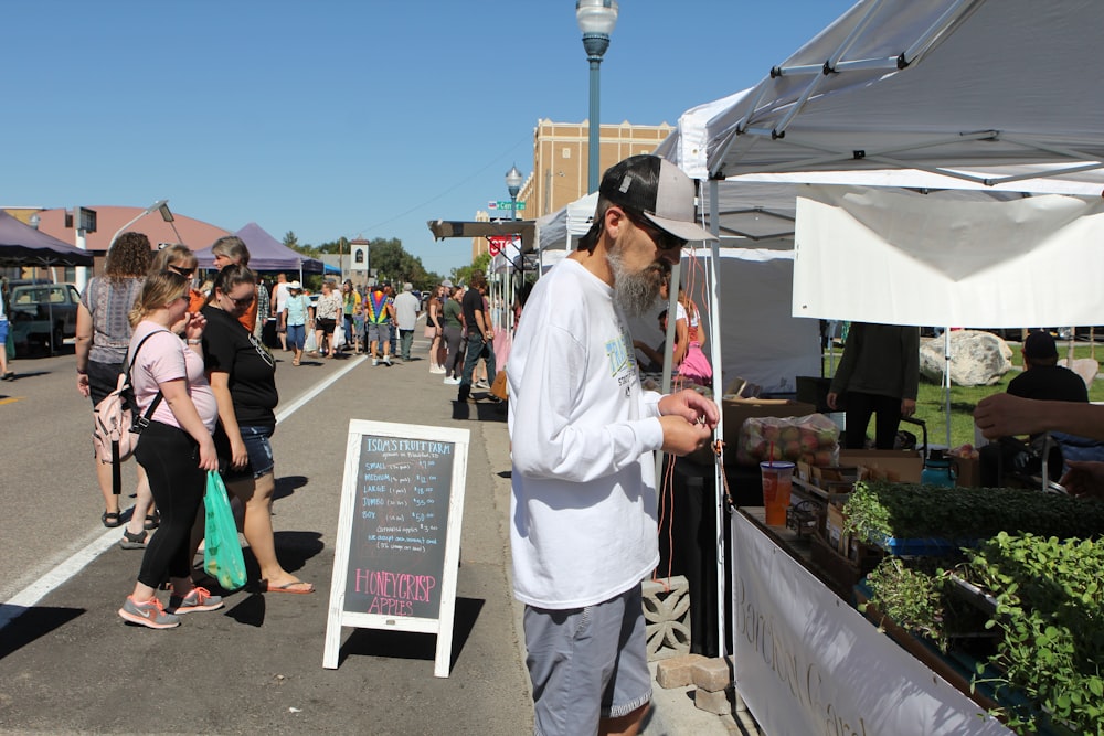 a man standing next to a sign at a farmers market