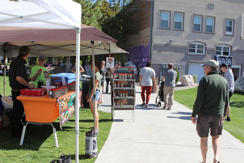 a group of people walking down a sidewalk next to a tent