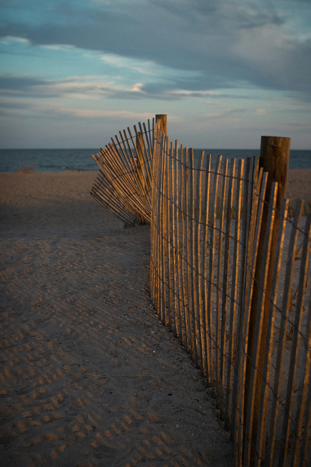 a wooden fence on a sandy beach next to the ocean