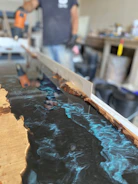 Hands carefully pouring resin into a mold, surrounded by resin supplies and tools.