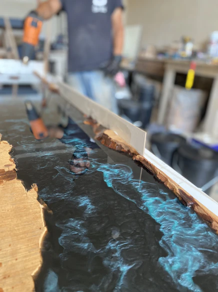 Artisan shaping a custom epoxy resin tabletop in a cozy workshop.