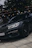 A sleek black luxury sedan parked curbside with city lights reflecting off its polished surface.