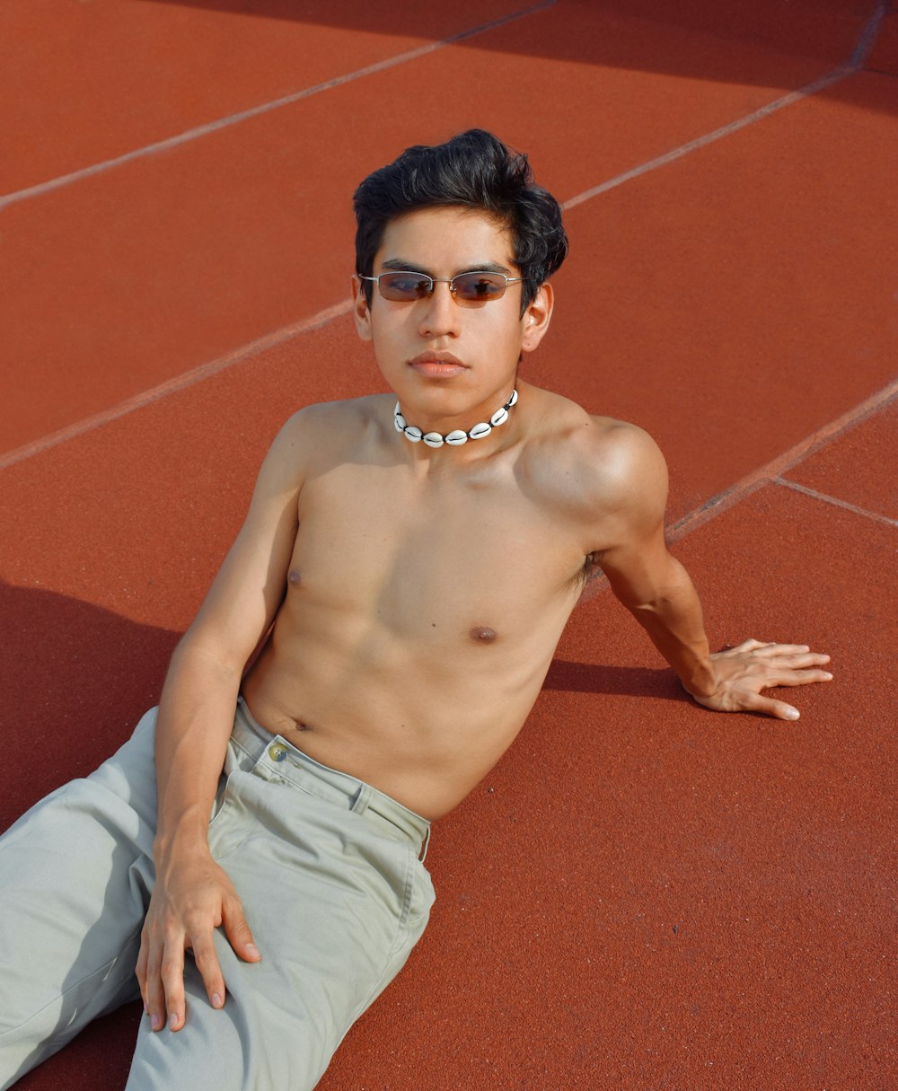 a shirtless young man sitting on a tennis court