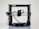 A 3D printer with a black frame and a visible extruder head equipped with wiring and motors. It rests on a clean, white surface with metal rods and a flat print bed for creating three-dimensional objects.