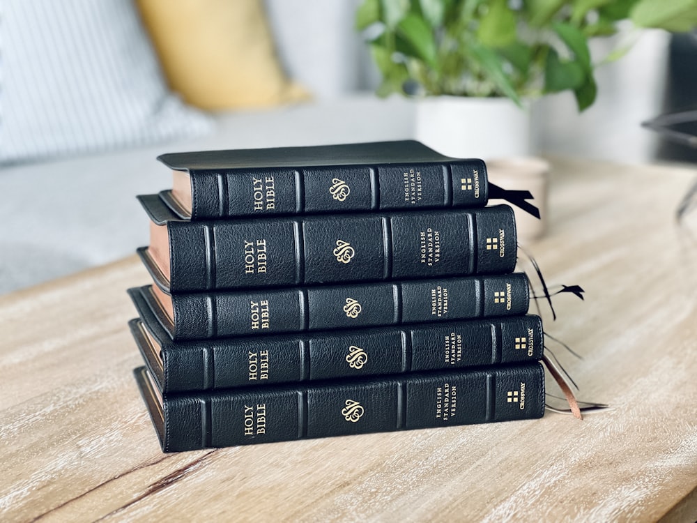 a stack of black books sitting on top of a wooden table