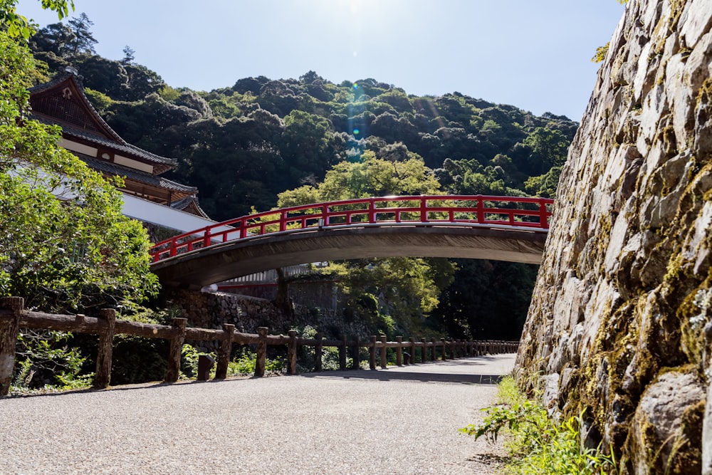 a red bridge over a river next to a lush green forest