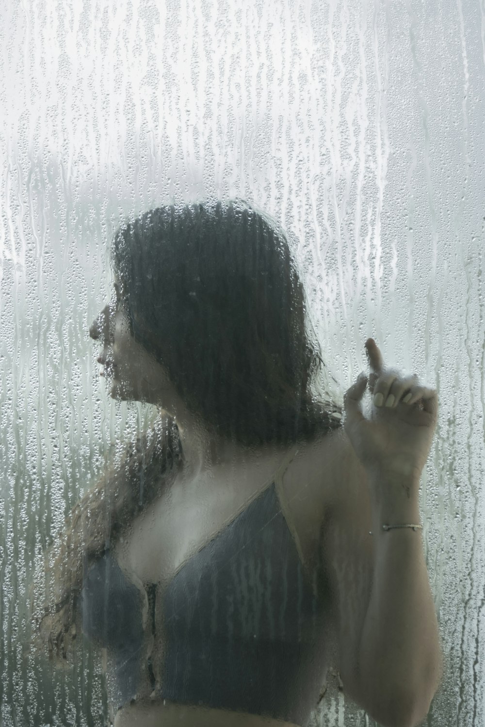 a woman standing in front of a window covered in rain