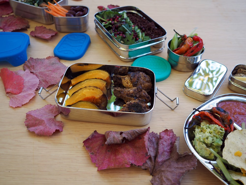 a wooden table topped with metal containers filled with food