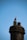 A bird, likely a seagull, stands on top of a chimney against a clear blue sky. The chimney is old and made of stone, with some visible wear and tear.