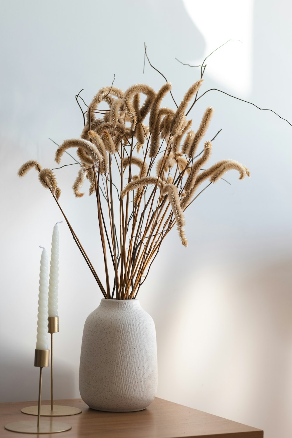 a white vase filled with dry grass on top of a wooden table