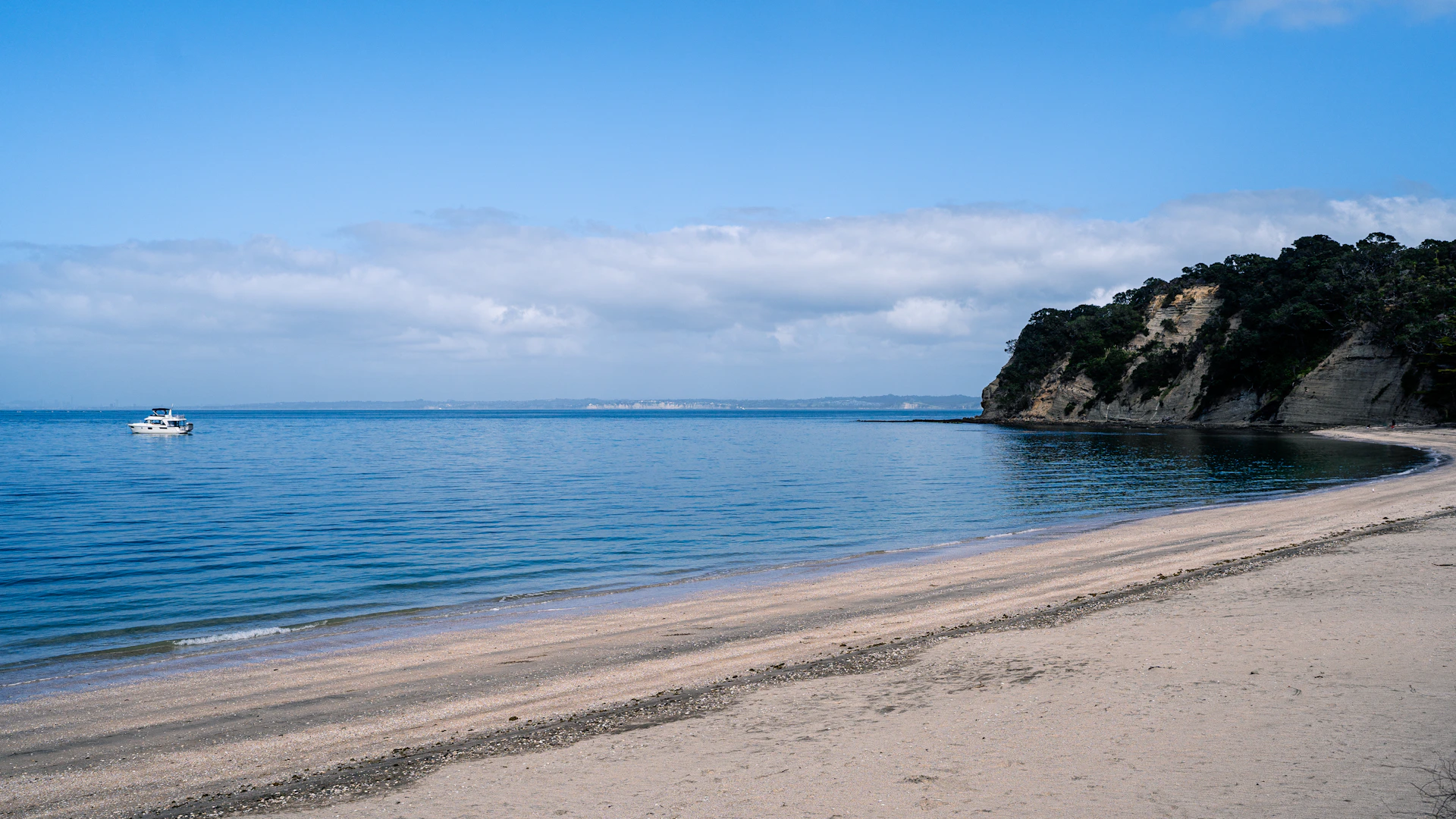 A serene beach scene with crystal-clear water, soft white sand, and a small fishing boat floating near the shore at dawn.
