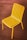 A bright yellow metal chair with a slatted design is positioned on a wooden deck. The wood planks have a rich brown color, with visible grain and joints adding texture to the background.