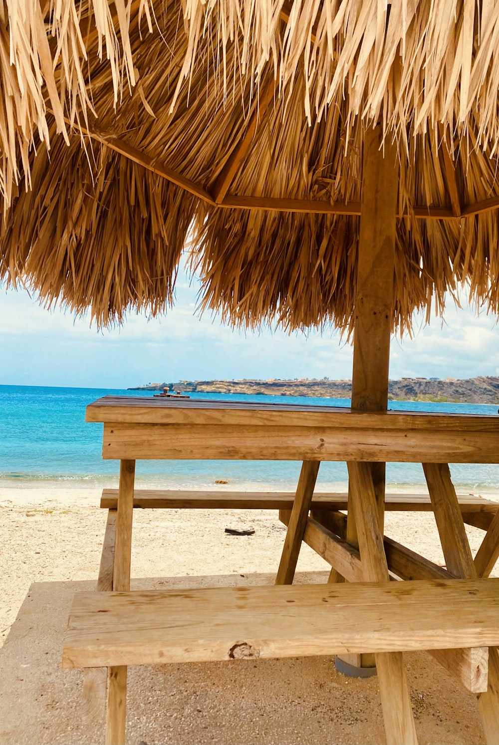 a wooden bench under a straw umbrella on a beach