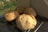 Four freshly baked loaves of bread are cooling on a metal rack placed on a dark kitchen counter. The loaves have a golden brown crust and are set against a backdrop of a garden, which is slightly out of focus in the background.