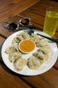 a white plate topped with dumplings next to a cup of sauce