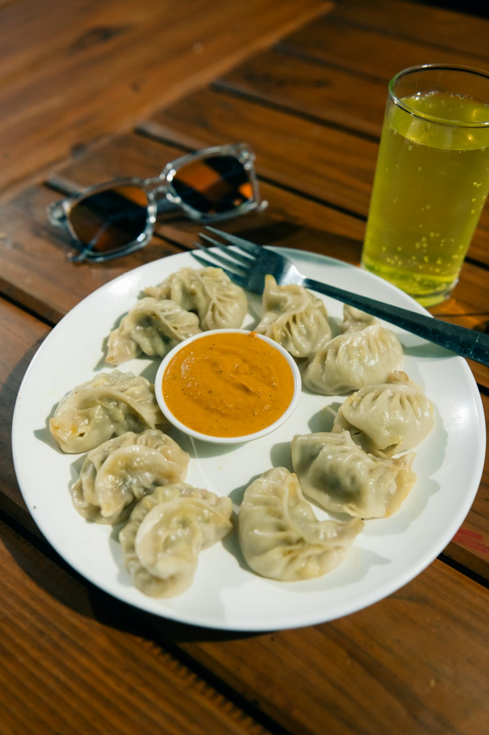 a white plate topped with dumplings next to a cup of sauce