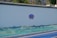 A large white wall with a decorative sign in the center. Below the wall is a section covered with a textured, green-blue surface that resembles waves or rolling hills. The ground in front is paved and features two distinct colors: blue and yellow.
