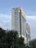 A high-rise building with the letters BKMEA on top, surrounded by other tall buildings and trees at the base. The sky is partly cloudy, and there are some cables visible in the foreground.