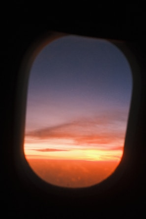 A vibrant sunset view from an airplane window showing fluffy clouds below.