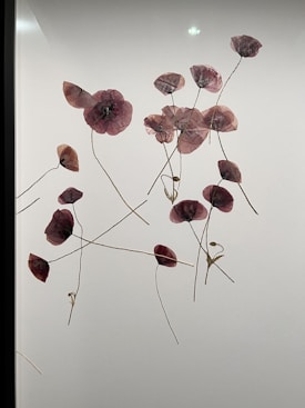 A collection of delicate, translucent flowers with thin, winding stems are pressed against a light background. The flowers are primarily purple with hints of pink and brown.