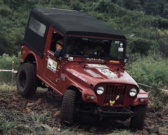 a red jeep driving down a muddy road