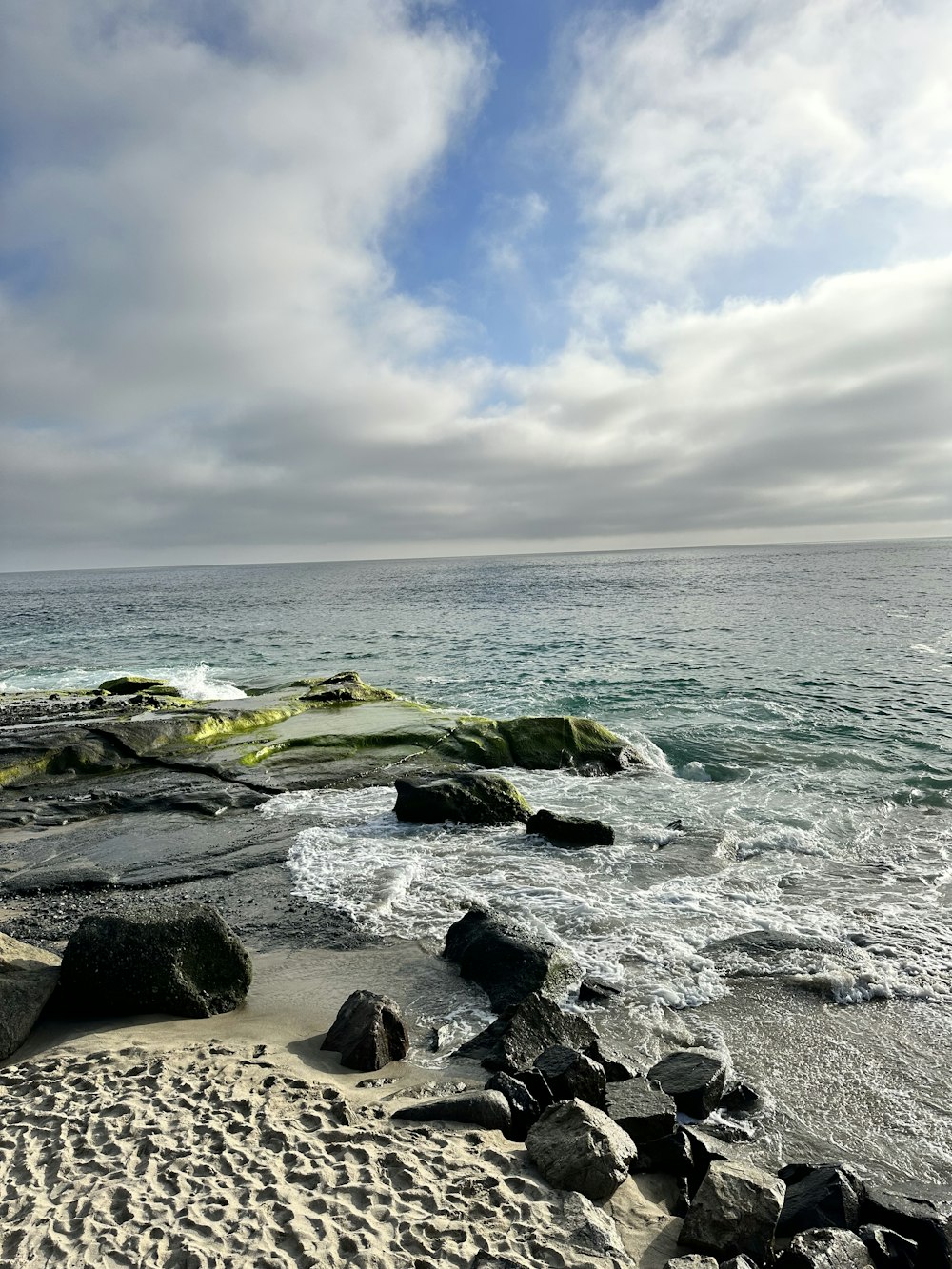 a sandy beach with rocks and water under a cloudy sky