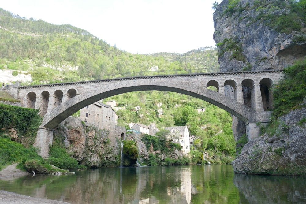 a stone bridge over a river next to a lush green hillside
