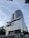 A modern, multi-story building with a sleek, metallic design. The facade features a large cylindrical structure with signage for a theme park. Glass windows and geometric patterns adorn the exterior, while palm trees add a touch of greenery at ground level.