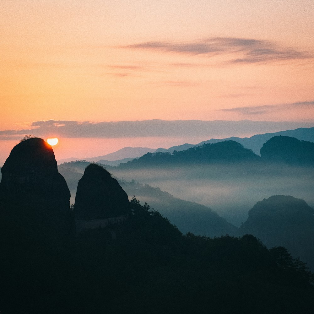 the sun is setting over the mountains in the fog