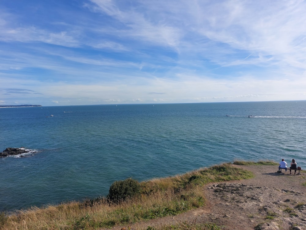 a couple of people sitting on top of a cliff near the ocean