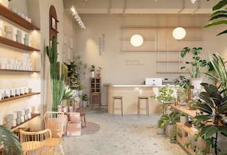 A well-lit, minimalist interior space with natural elements, featuring a variety of green plants and wooden furniture. There are shelves with white ceramic pots on the left, a large cactus, and additional plants scattered throughout. In the back, a wooden counter with stools sits beneath two spherical lamps. The walls are decorated with calming quotes and images, creating a serene and inviting atmosphere.