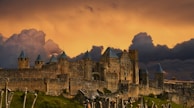 A moody landscape painting featuring a medieval castle at dusk.